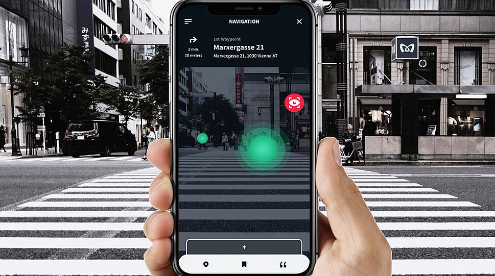 Das Bild zeigt die App-Oberfläche von Dreamwaves auf einem Smartphone vor dem Hintergrund eines Zebrastreifens. Ein oszillierender grüner Punkt markiert, woher das akustische Signal kommt.
