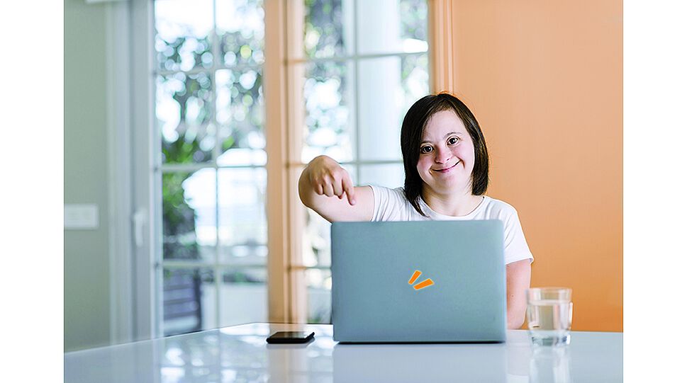 Mädchen sitzt an einem Tisch und zeigt auf Laptop