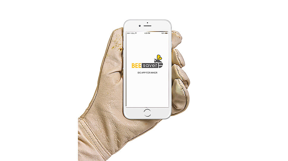 Hand mit Imkerhandschuh hält ein Smartphone, darauf am Bildschirm mit BeeSaver-Logo