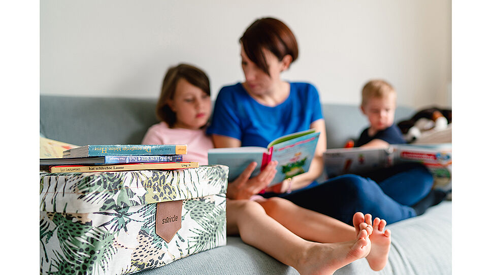 Swircle-Box - Mutter sieht mit den Kindern Bücher am Sofa an