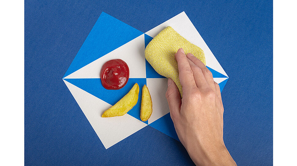 Eine Hand wischt Ketchup und zwei Pommes vom Teppich