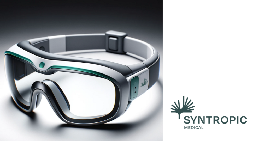 Das Bild zeigt ein futuristisches Brillengerät mit einem breiten Kopfband. Die Brille hat große, gebogene Gläser, die an eine Schutz- oder Skibrille erinnern, und ist mit einer grauen Umrandung versehen. Links am Kopfband ist das Logo von Syntropic zu erkennen, das ein Palmblatt darstellen soll. Oberhalb der Gläser, im Bereich der Stirn, befindet sich ein leuchtend grüner Streifen. Das Design ist schlank und wirkt technologisch fortgeschritten. © Syntropic